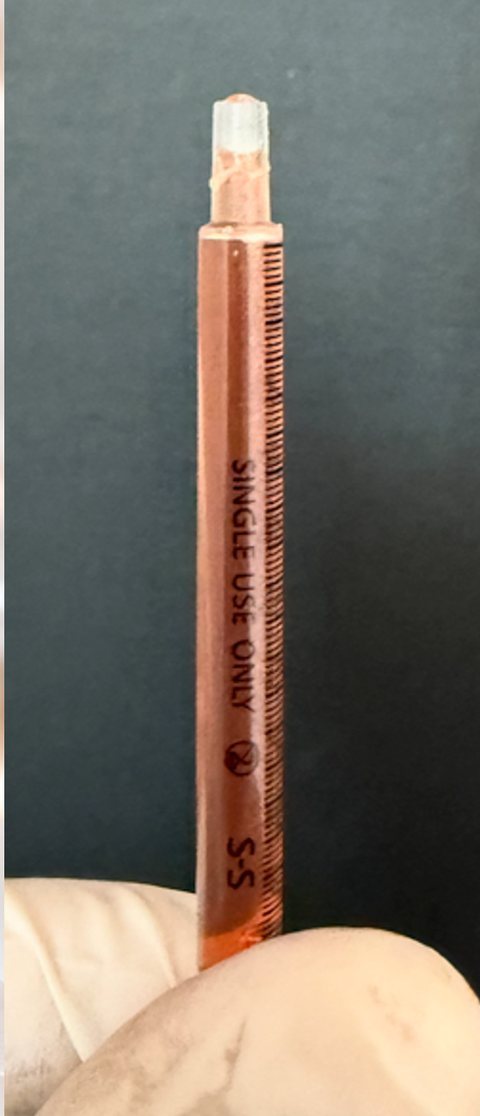 A thin single-use syringe filled with orange fluid